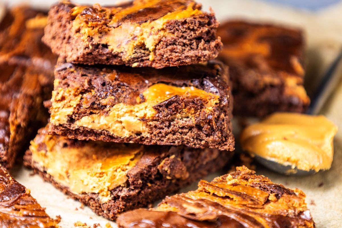 A stack of chocolate and peanut butter brownies on parchment paper, with a spoonful of peanut butter beside them.