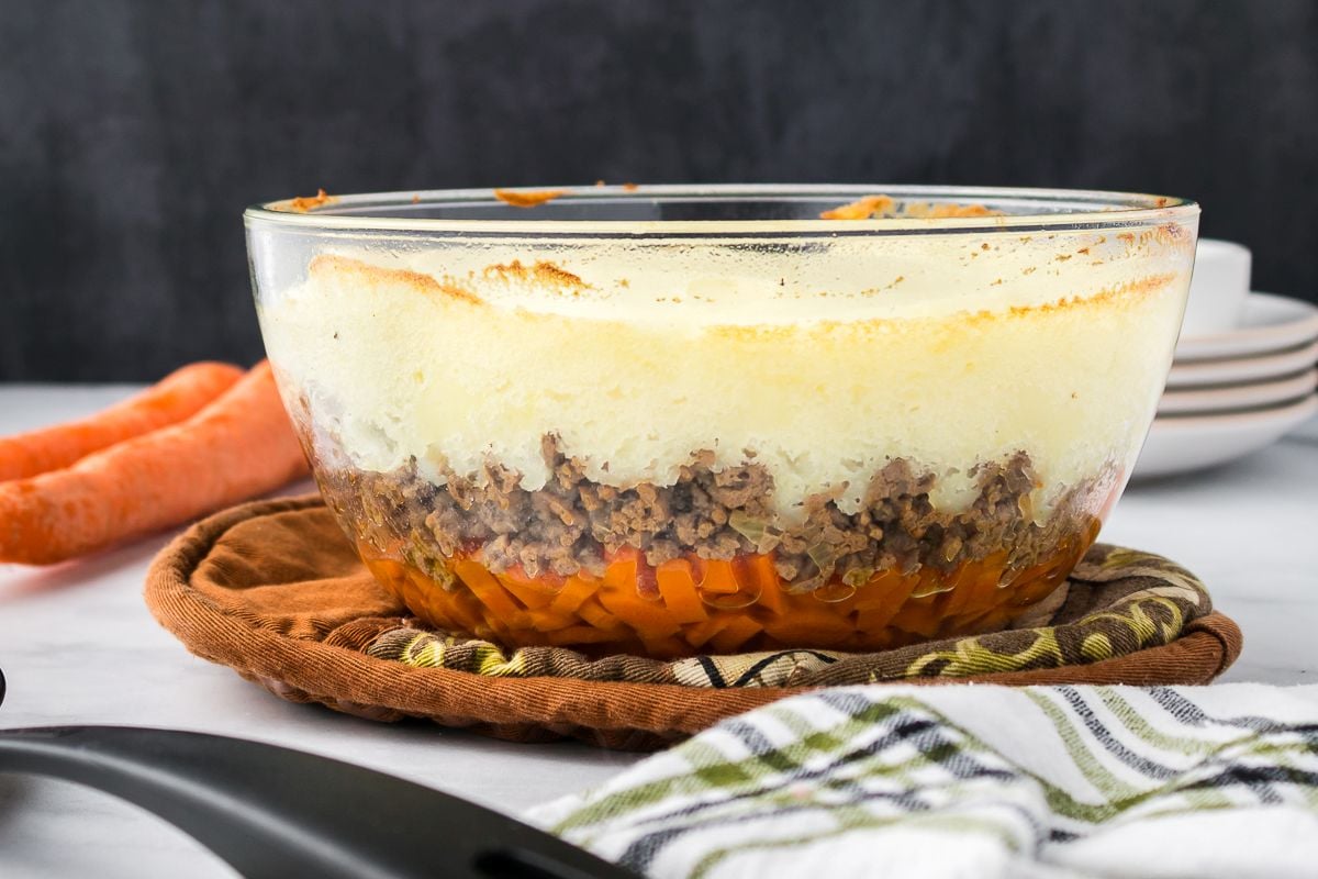 Side view of clear bowl layered with carrots, ground beef, and mashed potatoes.
