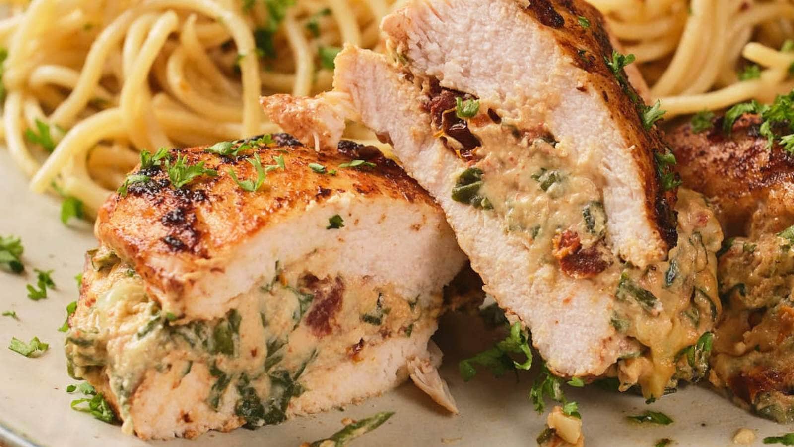 A white plate of air fryer stuffed chicken breast with cooked pasta, and a fresh parsley next to it on a white surface.