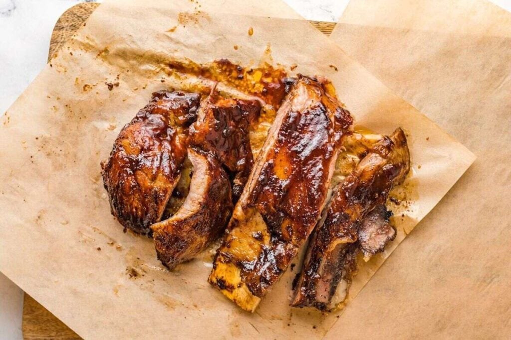 Barbecued pork ribs sliced on parchment paper, showing a glazed, caramelized surface and tender meat.