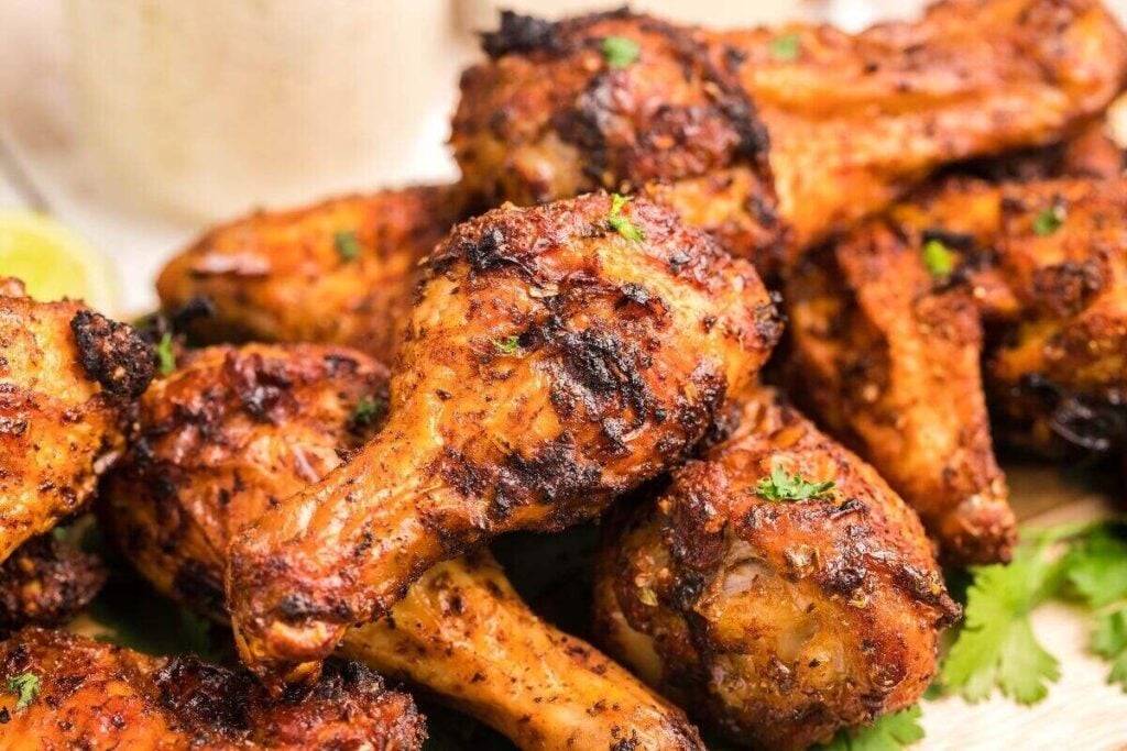 A close-up view of several grilled chicken drumsticks seasoned with spices and garnished with chopped herbs.
