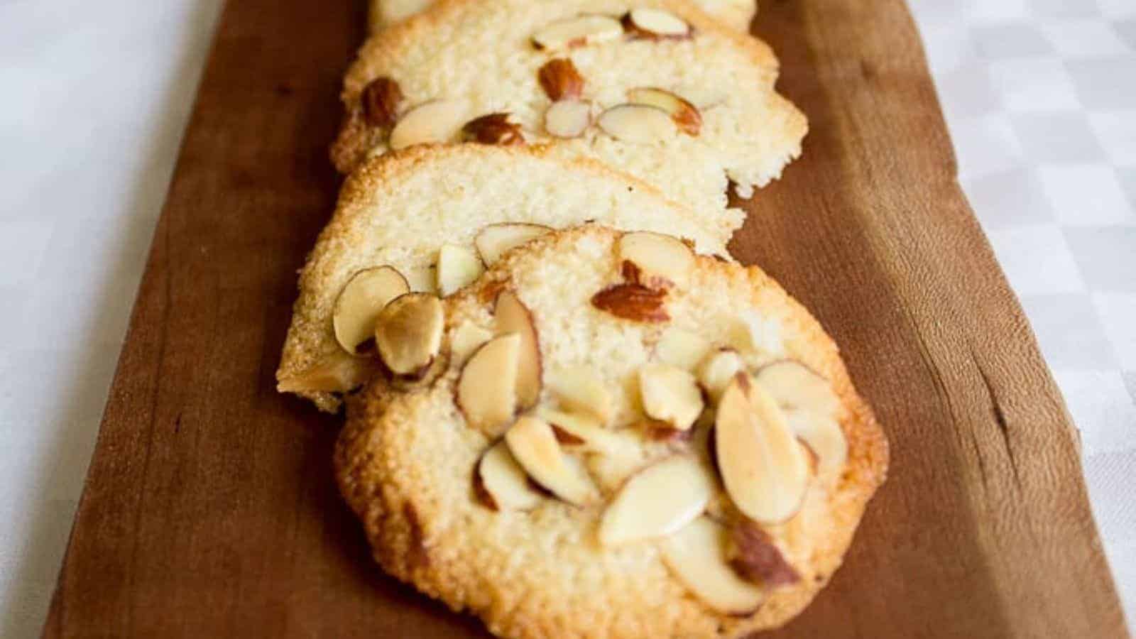 Thin, crisp almond tuile cookies topped with sliced almonds, on a wooden serving board.