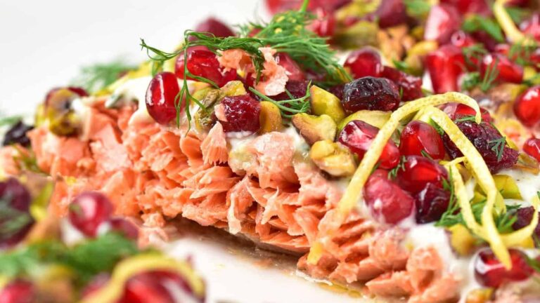 Close-up of cooked salmon topped with pomegranate seeds, pistachios, dill, and lemon zest.