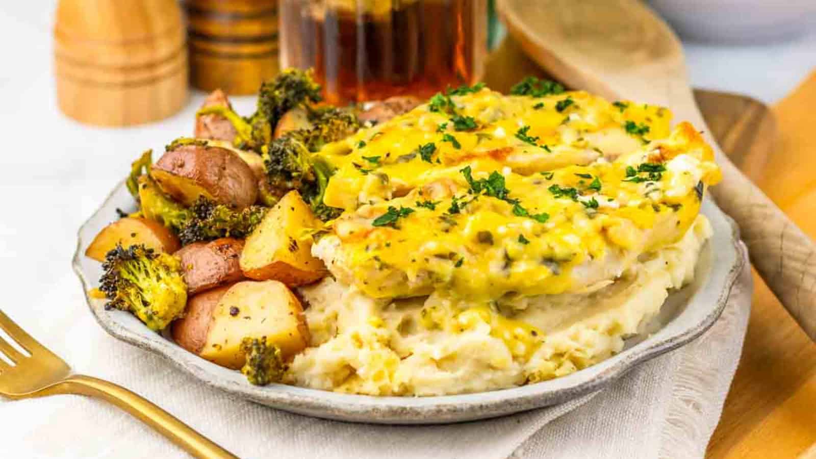 A plate of mashed potatoes, baked chicken with sauce, and roasted potatoes with broccoli, garnished with herbs.