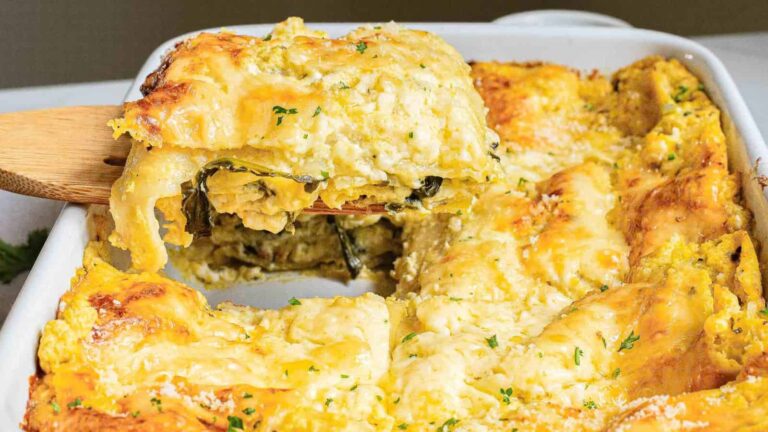 A slice of cheesy baked lasagna being lifted from a casserole dish, showing layers of pasta, sauce, and spinach.