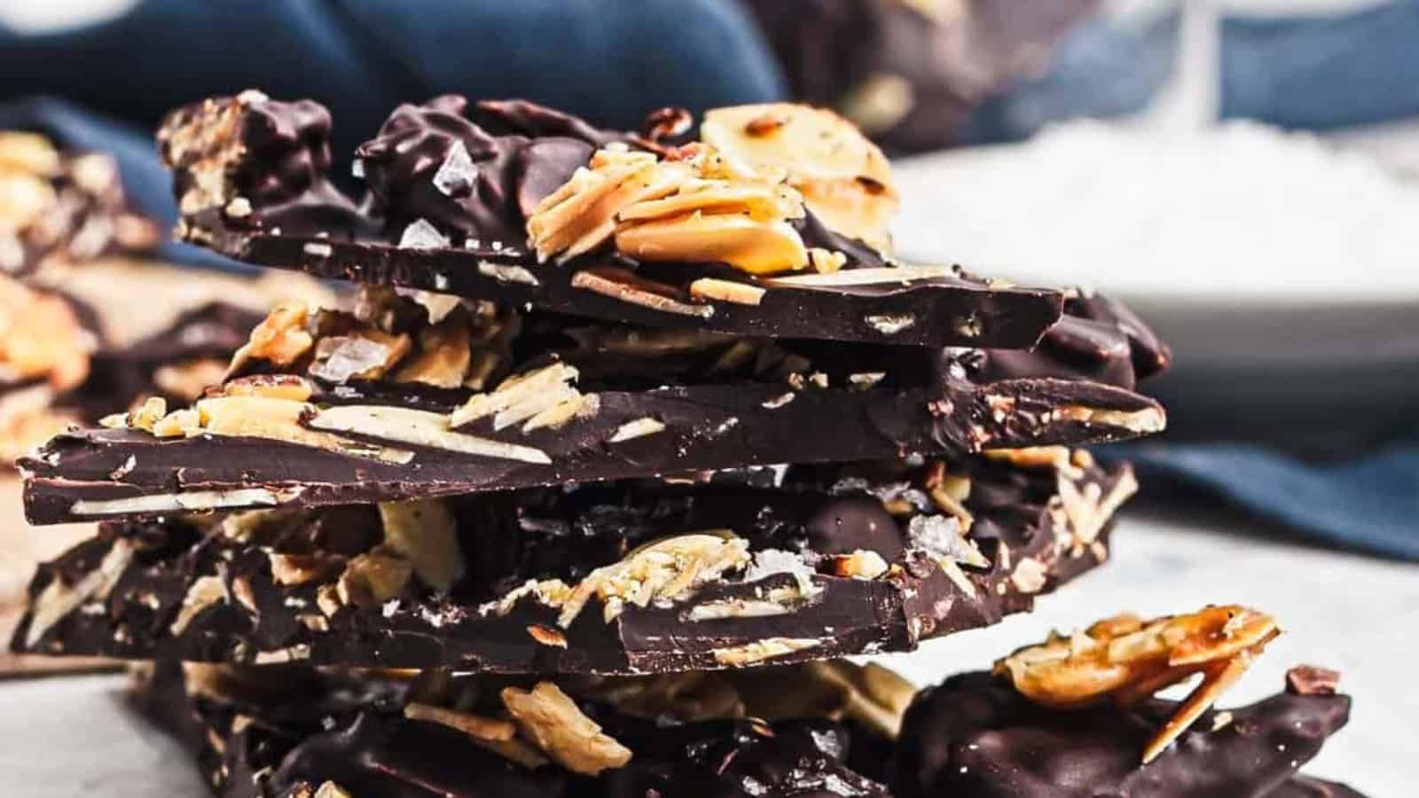 A stack of dark chocolate bark with almonds and sea salt on a marble surface.