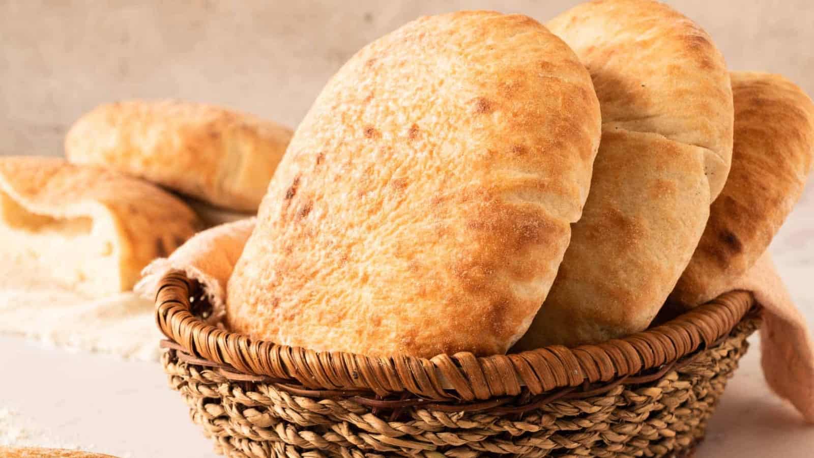A basket filled with several pieces of freshly baked pita bread on a light surface.