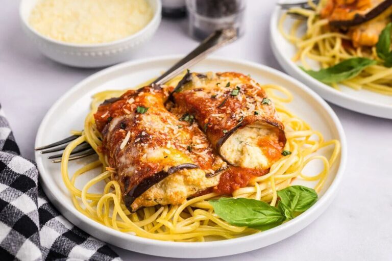 A plate of spaghetti topped with eggplant rollatini filled with ricotta cheese, marinara sauce, grated cheese, and a basil garnish.
