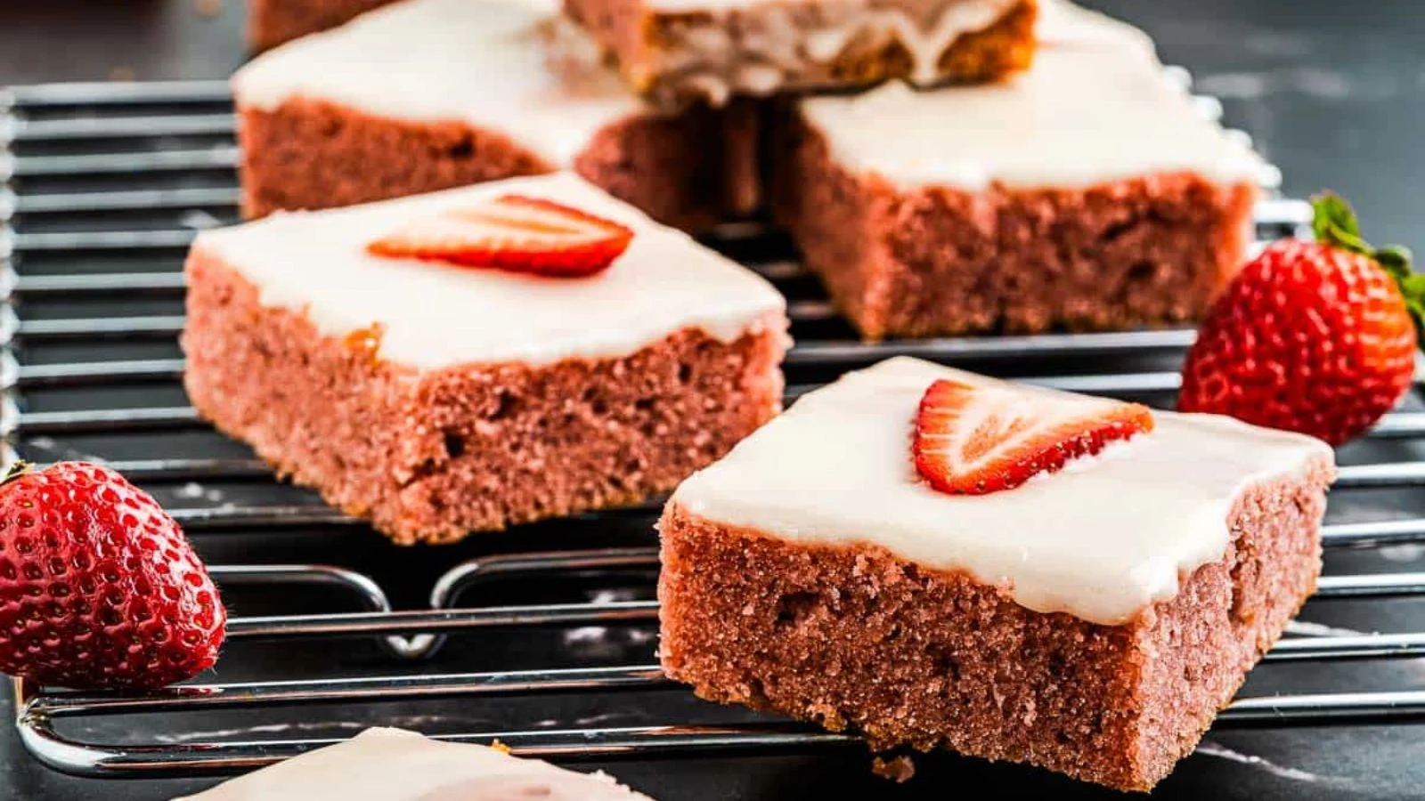 Fudgy strawberry brownies topped with pink glaze and fresh strawberry pieces.