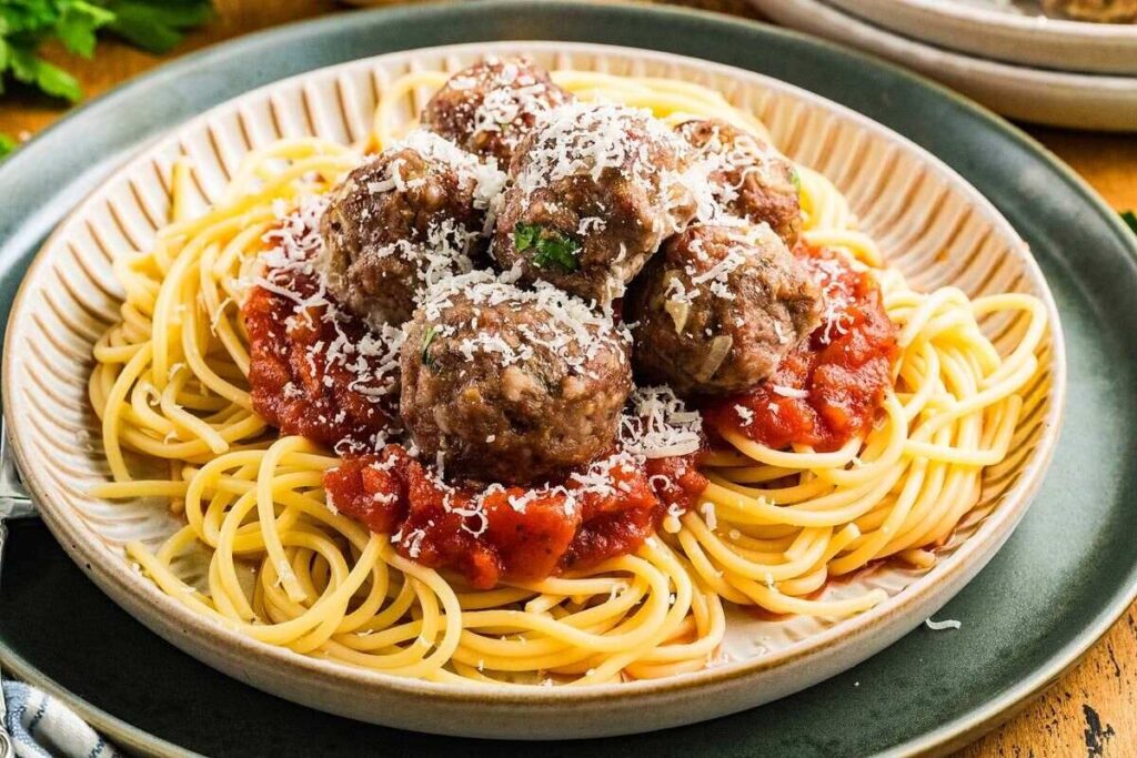 A plate of spaghetti topped with tomato sauce, several meatballs, and grated cheese.