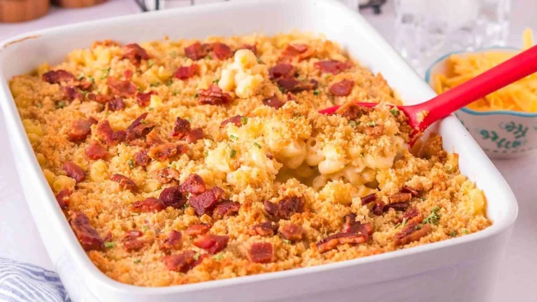 Baked macaroni and cheese casserole topped with breadcrumbs and bacon, served in a white dish with a red serving spoon.