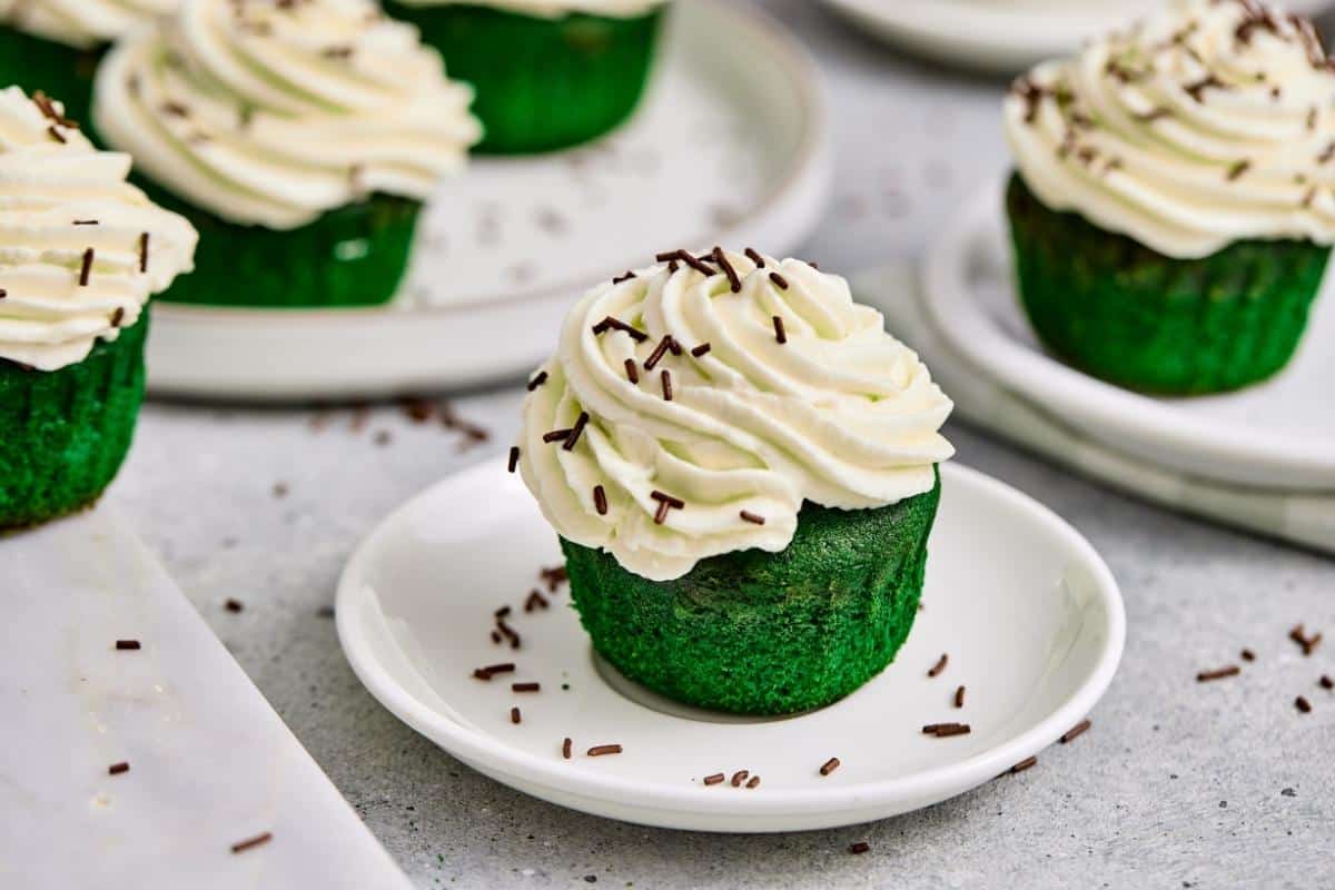 A St. Patrick’s Day Green Matcha Cupcakes sits on a small white plate, with more cupcakes visible in the background.