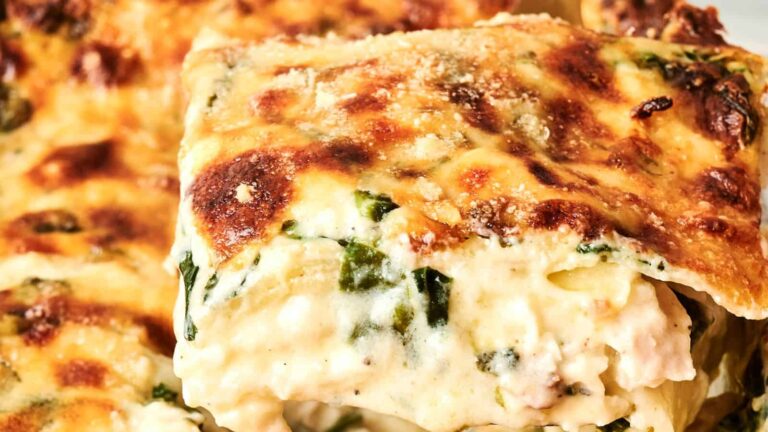 Close-up of a slice of baked white lasagna with visible layers of pasta, creamy cheese sauce, and spinach, topped with a browned cheese crust.