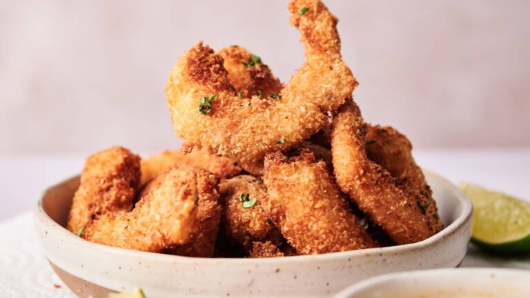 A bowl of golden-brown breaded and fried shrimp garnished with chopped herbs, with a lime wedge partially visible on the side.