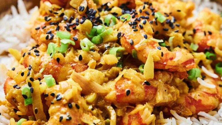 Close-up of shrimp curry with chopped green onions and black sesame seeds, served over a bed of white rice.