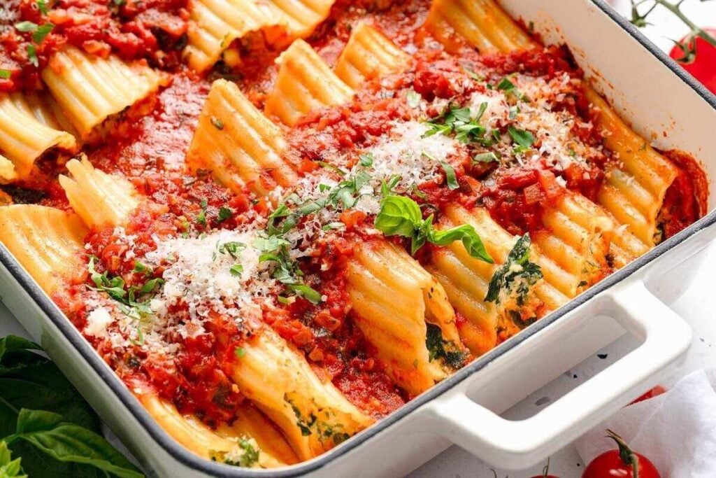 Baked manicotti pasta stuffed with spinach and cheese, topped with tomato sauce, grated cheese, and fresh herbs in a white rectangular baking dish.