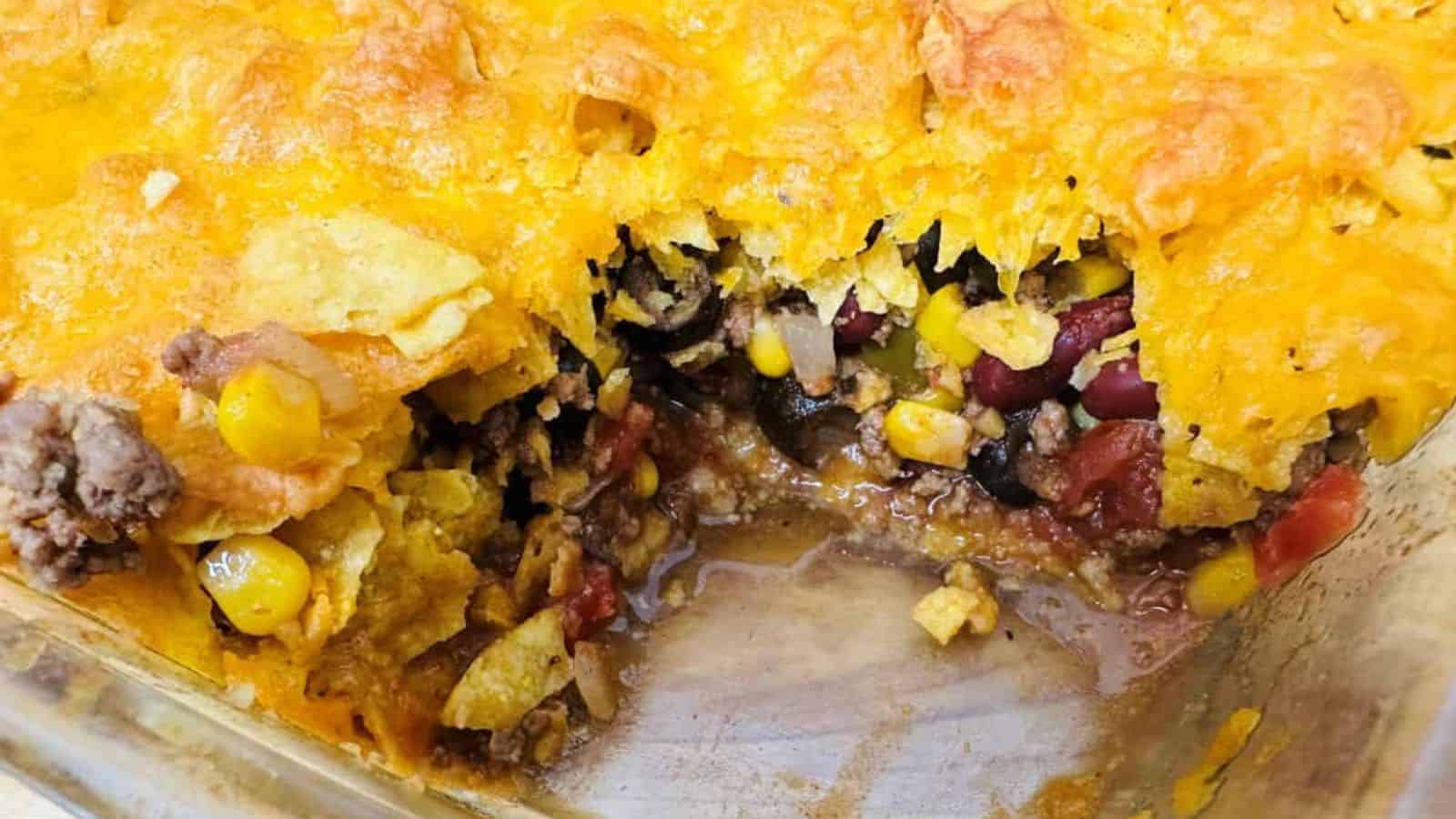 A partially served Mexican casserole in a baking dish, showing layers of corn, beans, cheese, and ground meat.