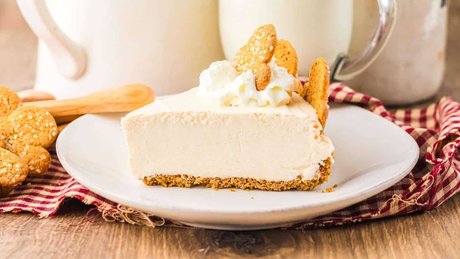 A slice of creamy cheesecake with whipped cream and cookies on top, served on a white plate.