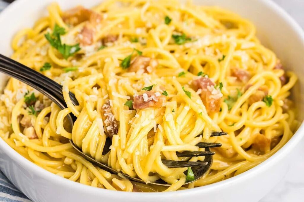 A bowl of pasta alla carbonara topped with chopped parsley and grated cheese, with a fork twirling some pasta.