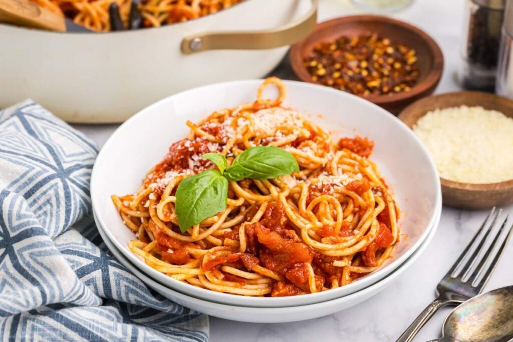 A bowl of pasta amatriciana with tomato sauce, garnished with basil and Parmesan cheese. 