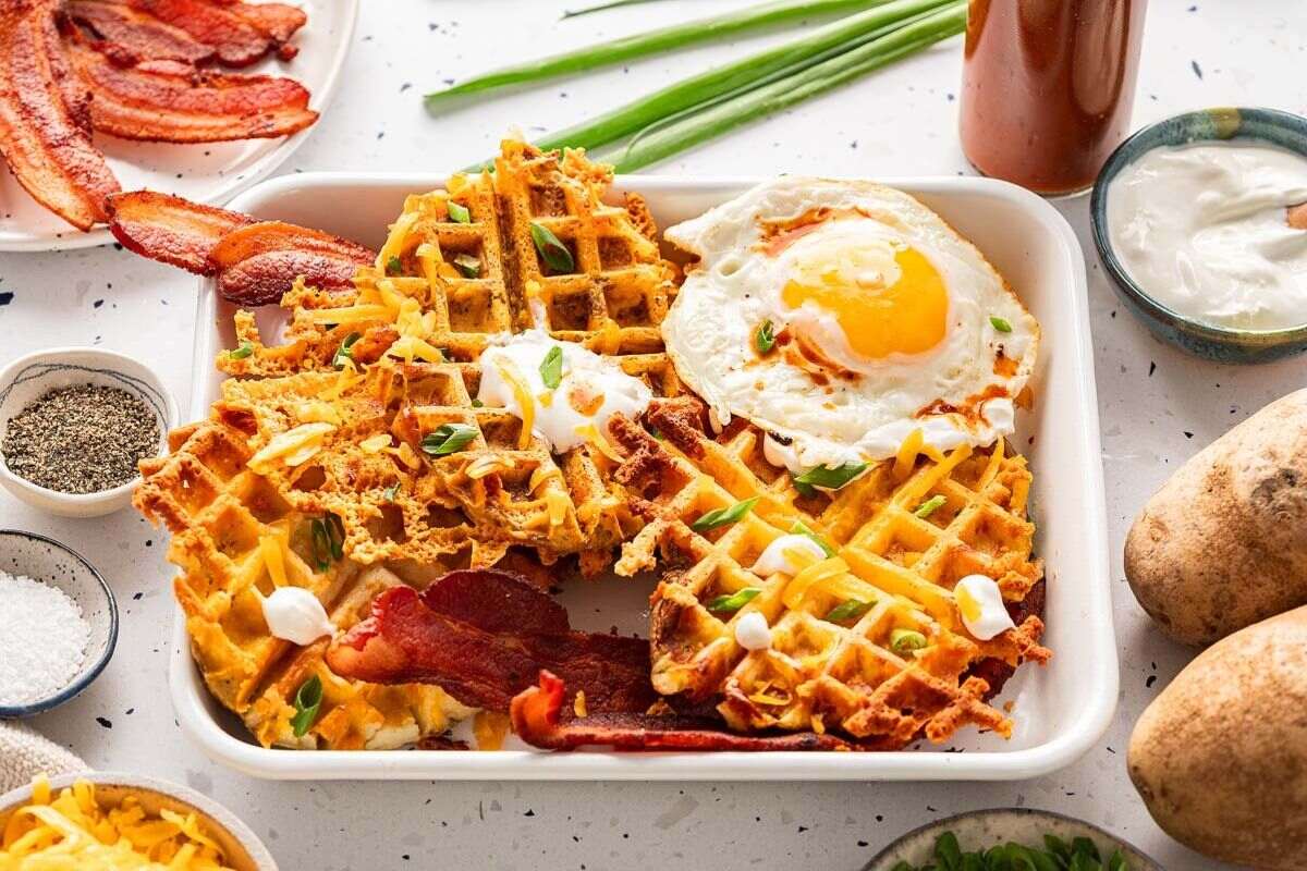 A tray full of waffles, bacons and sunny side up egg.
