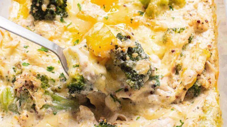 Close-up of a cheesy broccoli and chicken casserole with a spoon lifting a portion, showing melted cheese, broccoli florets, and pieces of chicken.