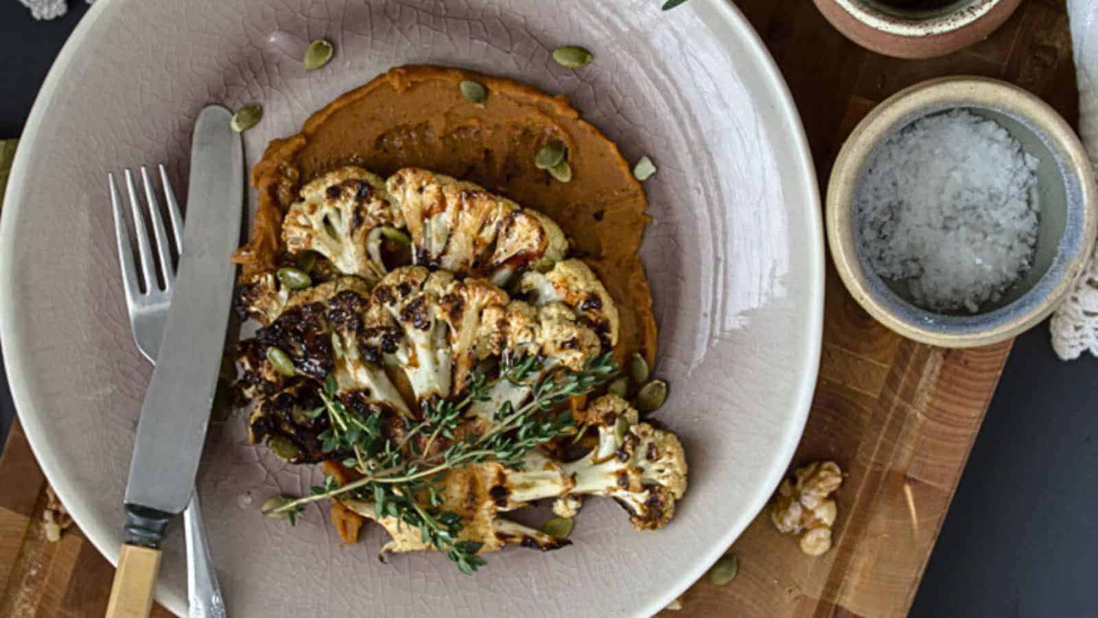 A dish with roasted cauliflower slices on a bed of reddish-brown puree, garnished with thyme and pumpkin seeds.