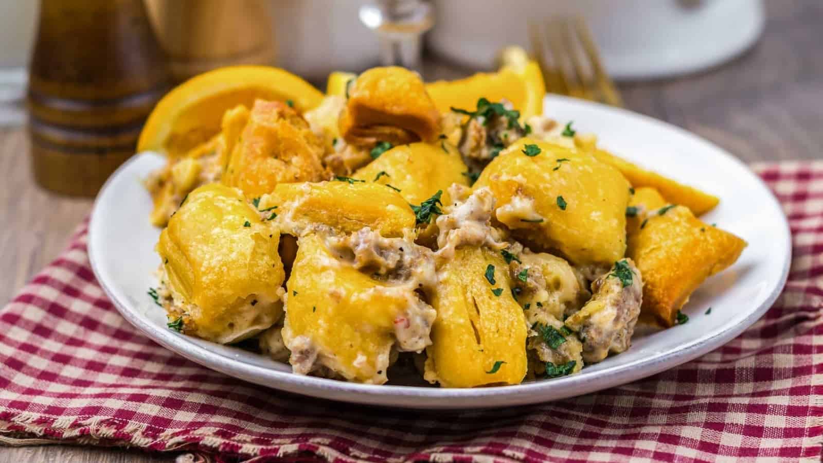 A plate of crispy roasted potatoes topped with creamy sauce and herbs, on a red checkered napkin.