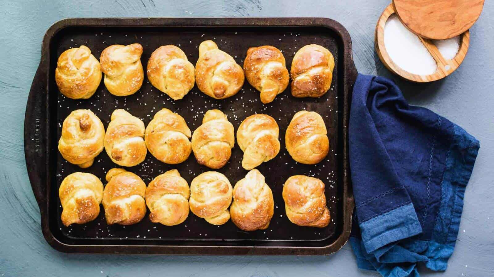 Golden brown soft pretzel knots on a baking sheet.