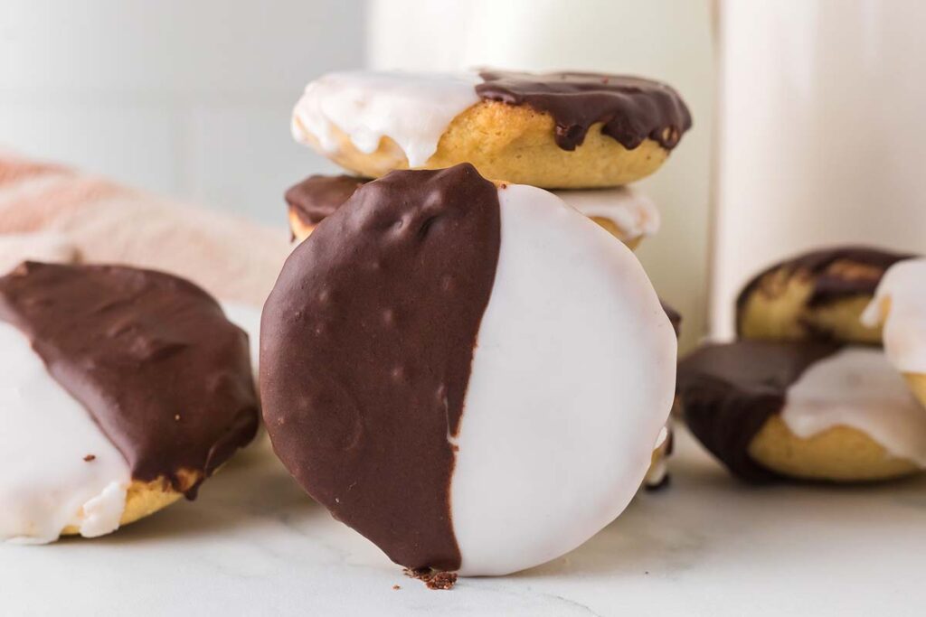 A stack of black and white cookies, each half-covered in chocolate icing and half in white icing, sits on a white surface.