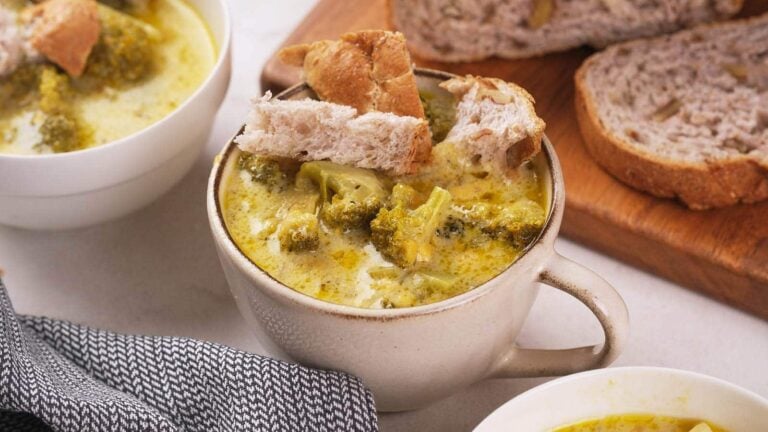 A ceramic mug filled with broccoli soup, topped with pieces of bread.