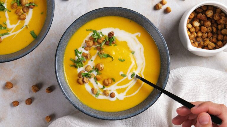 A bowl of creamy yellow soup garnished with a swirl of cream.