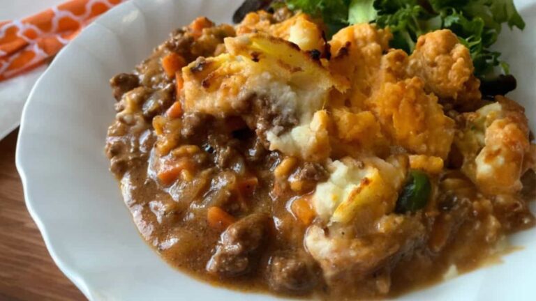 A plate of shepherd's pie with ground meat, vegetables, and mashed potatoes, served with a side of mixed greens.