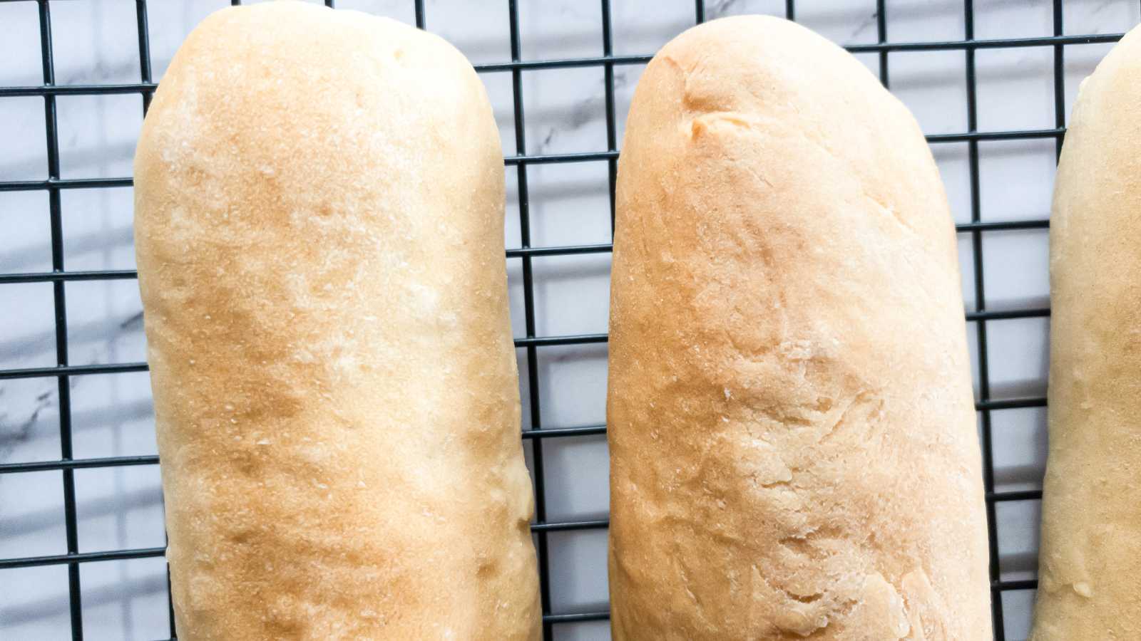 Two loaves of jimmy johns bread cooling on a wire rack with a marble surface in the background.