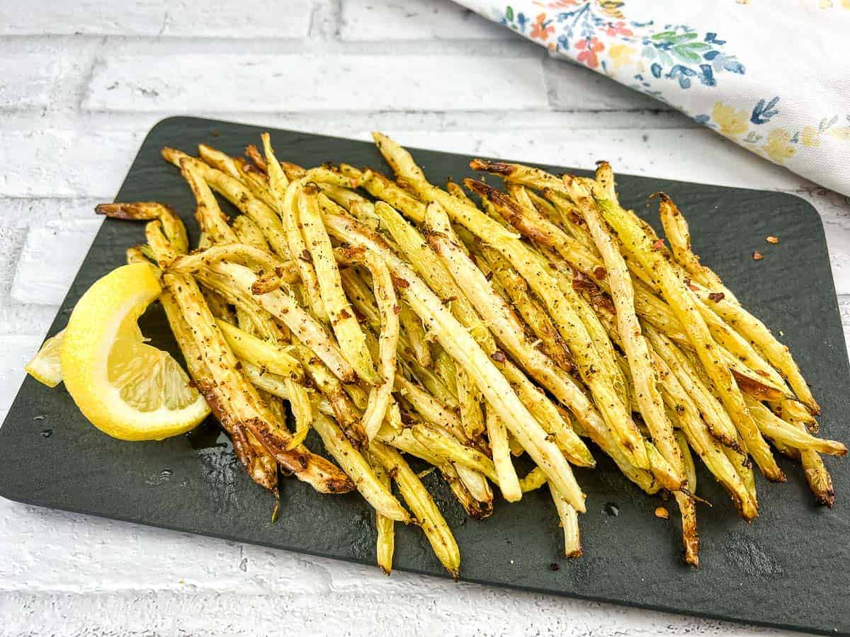 Lemon pepper yellow beans on a black plate with lemon wedges.