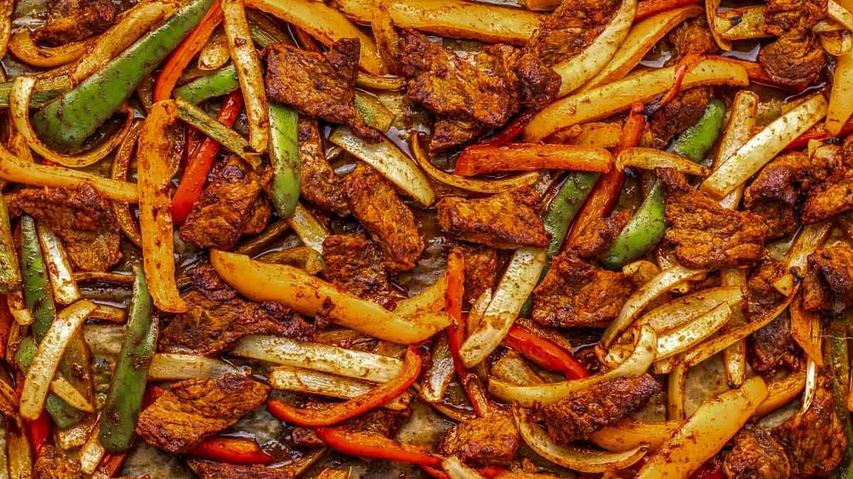 Sliced bell peppers, onions, and seasoned beef strips arranged on a baking sheet.