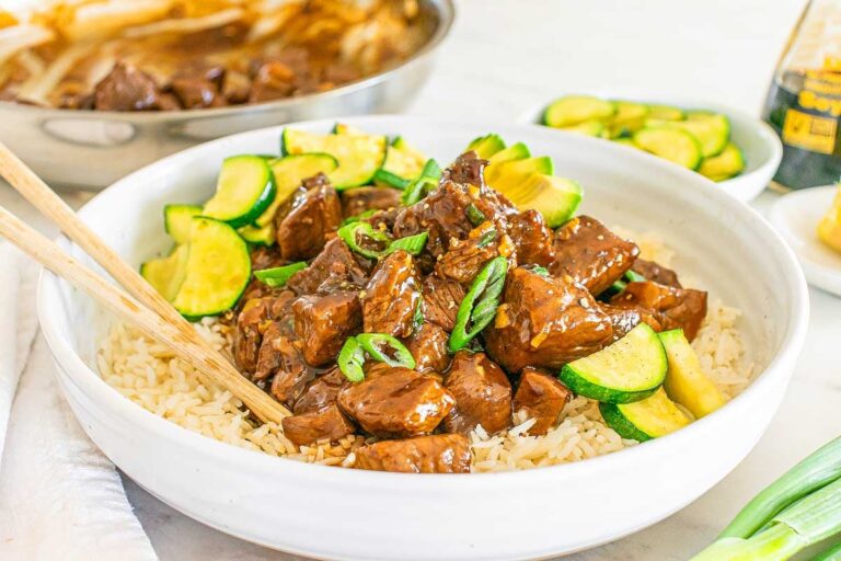 A bowl of teriyaki steak bite stir-fry with zucchini served over rice, garnished with green onions.