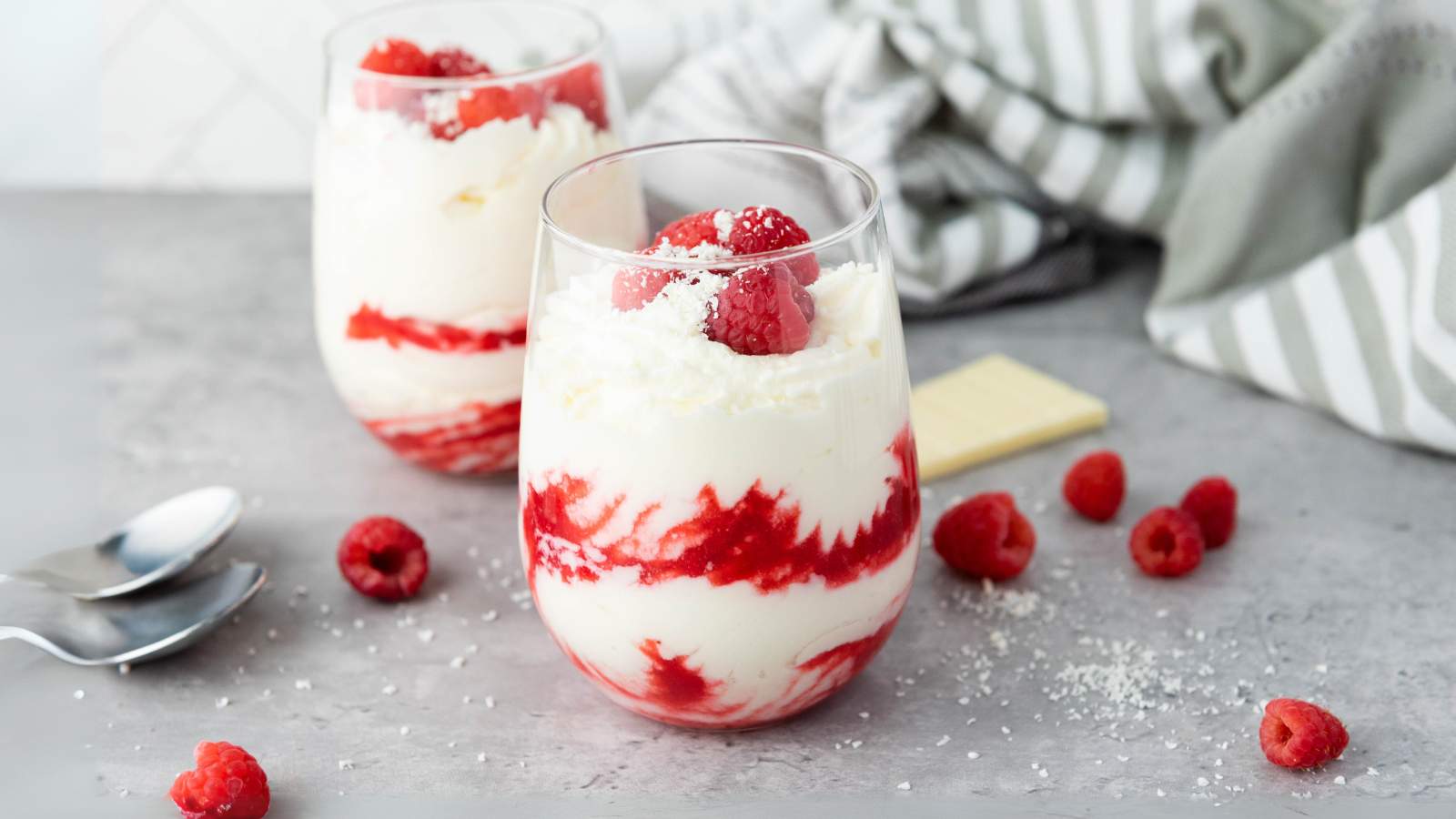 Two glasses of white chocolate mousse, topped with raspberries and white chocolate.
