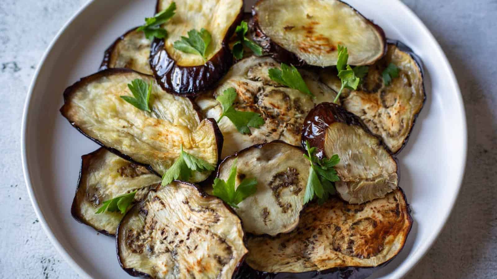 Sliced roasted eggplant garnished with fresh parsley on a white plate.