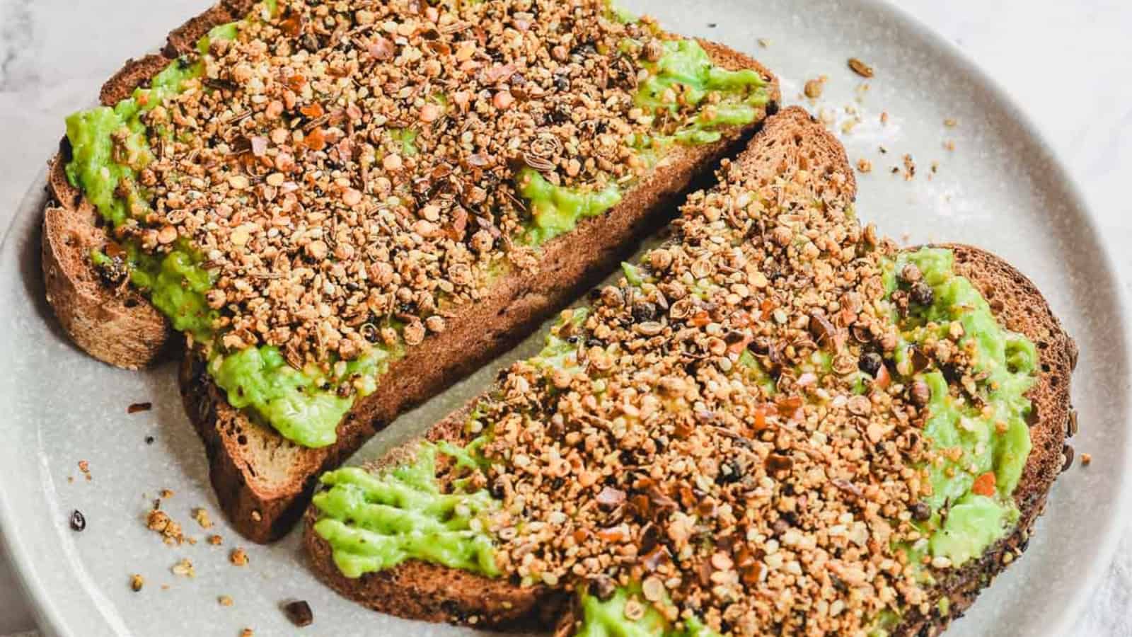 Two slices of toast topped with mashed avocado and sprinkled with mixed seeds on a plate.