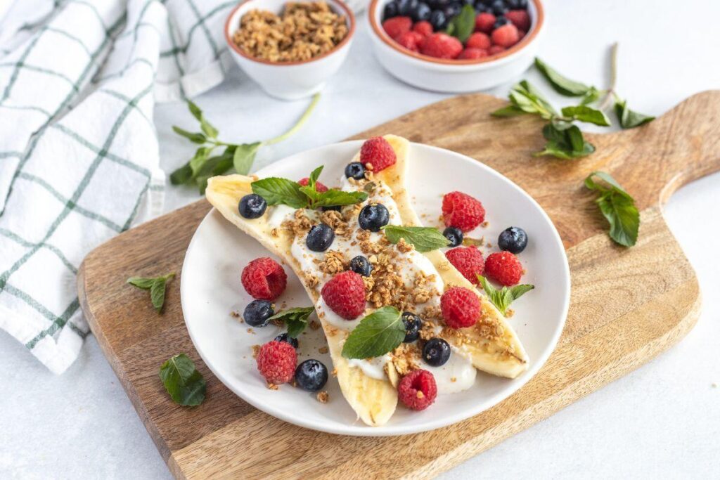 Breakfast Banana Split: A healthy breakfast idea for kids featuring yogurt, granola, raspberries, blueberries, and mint on a banana.