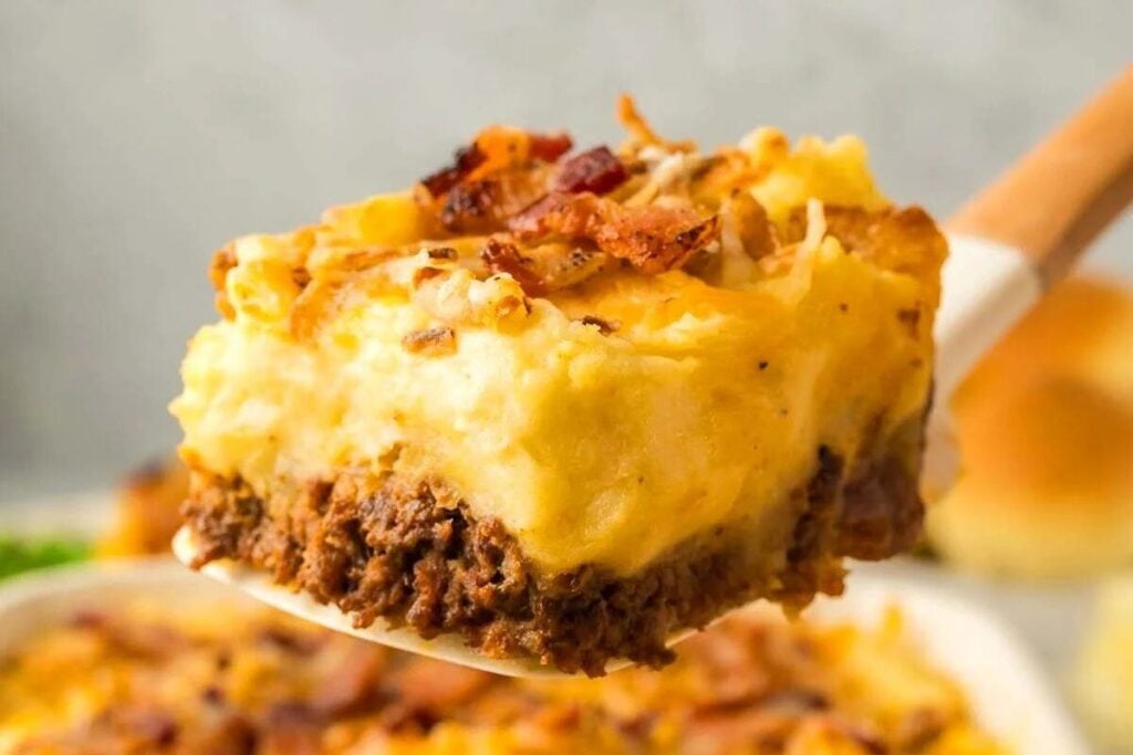 A slice of cowboy meatloaf and potato casserole topped with melted cheese and bacon.