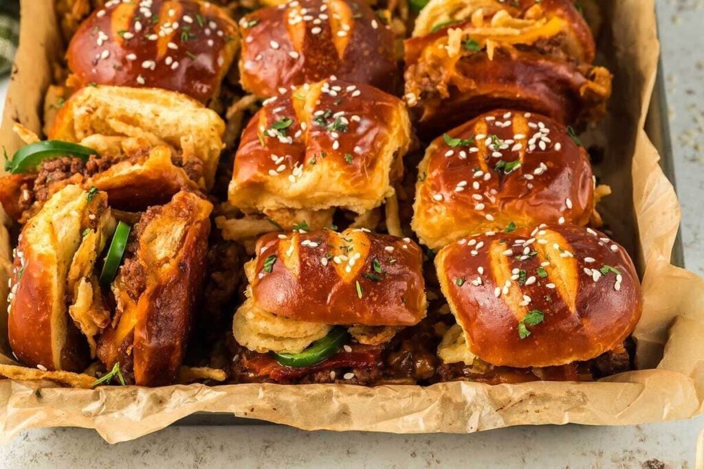 A tray of cowboy sliders with pretzel buns, crispy chicken, crispy fried onions, and a sprinkle of sesame seeds.