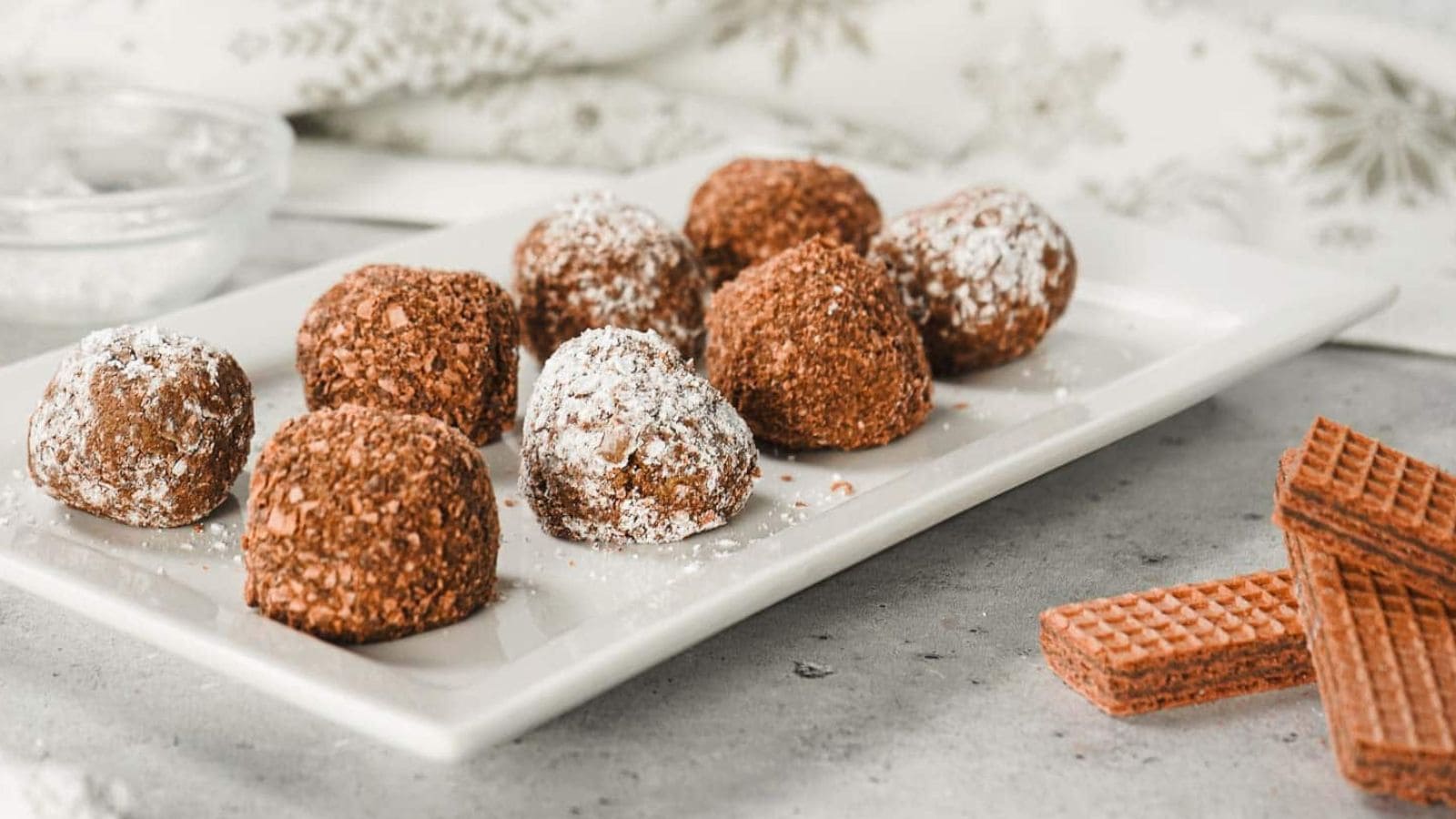 Chocolate truffles dusted with powdered sugar on a white plate, with wafer biscuits beside them.