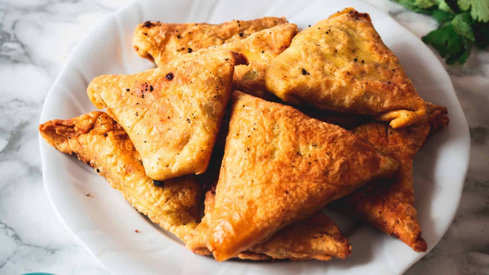 Golden-brown triangular samosas on a white plate.