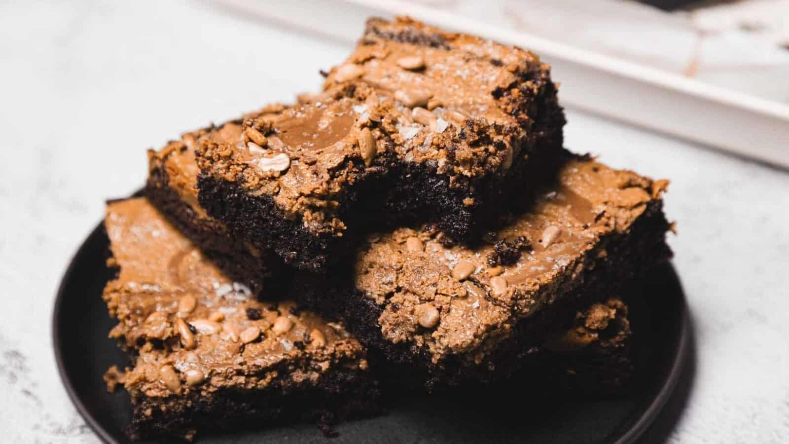 A stack of fudgy chocolate brownies with a cracked top, served on a black plate.