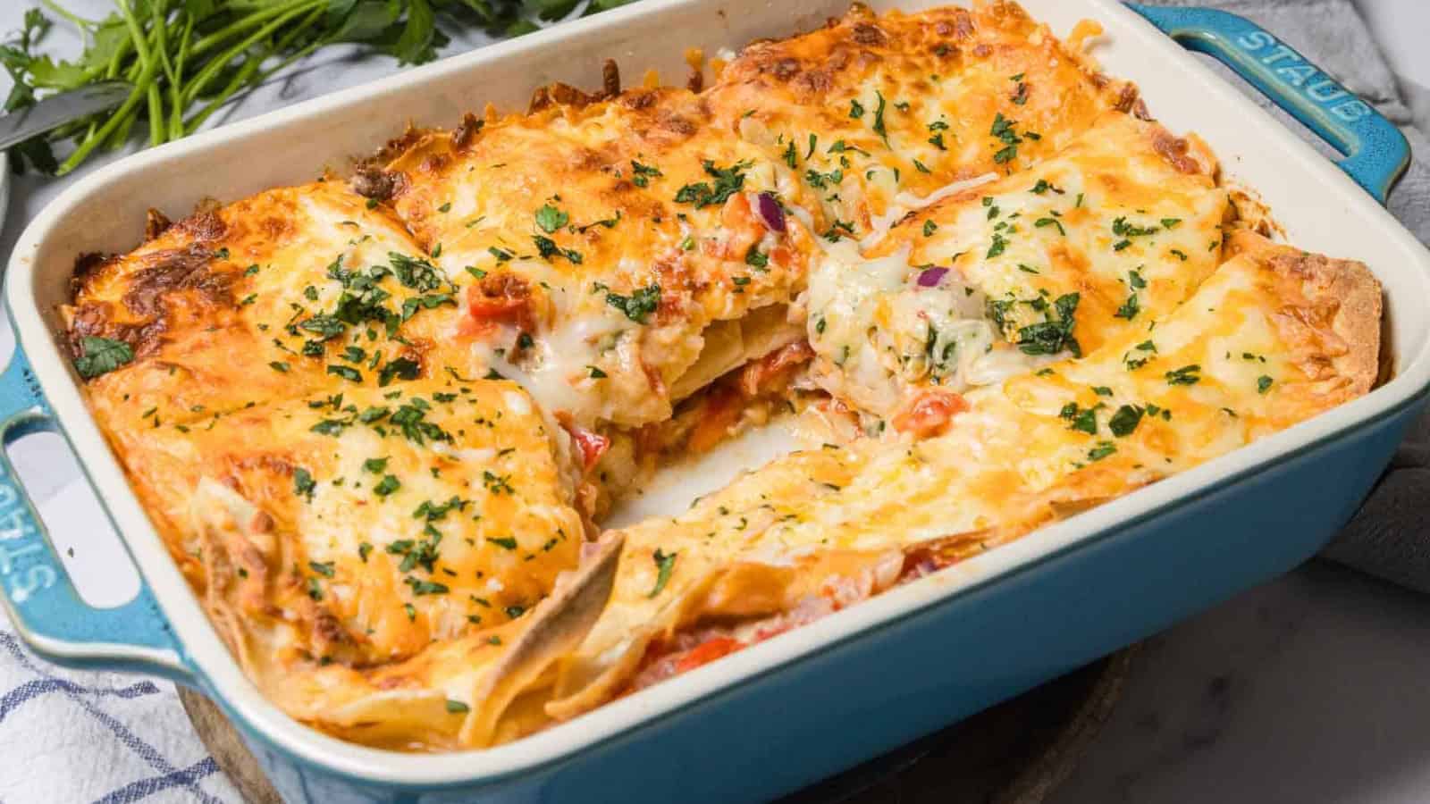 A cheesy baked lasagna in a blue dish, with a square piece removed and herbs sprinkled on top.