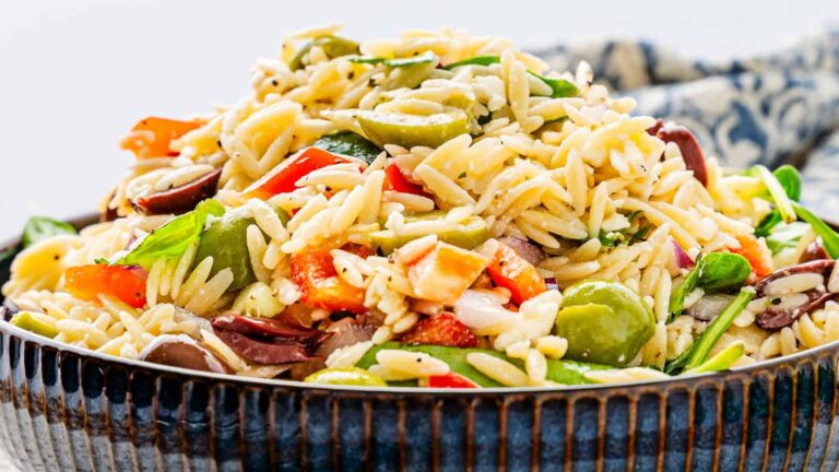 A bowl of orzo salad with mixed vegetables, including olives, tomatoes, and spinach, garnished with herbs.