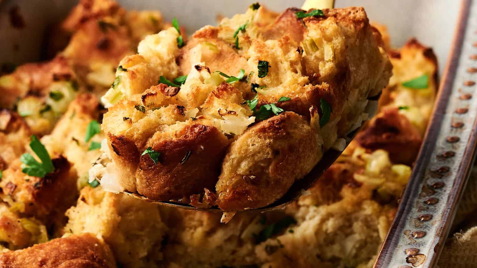 A close-up of a serving of bread stuffing with chopped herbs, lifted from a baking dish.