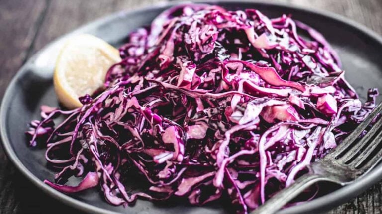 Shredded red cabbage salad on a dark plate with a lemon wedge and a fork.